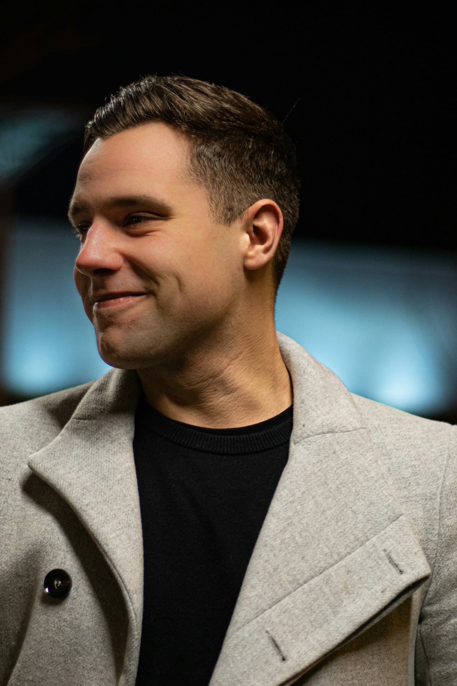 A man in a grey coat smiles as he looks back across at her