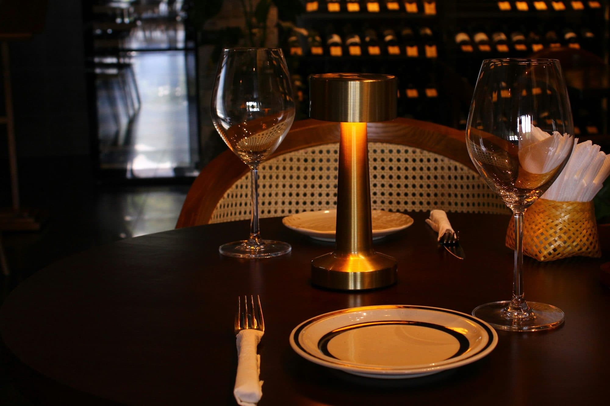 A small table set for two, with two wine glasses and a warm brass lamp